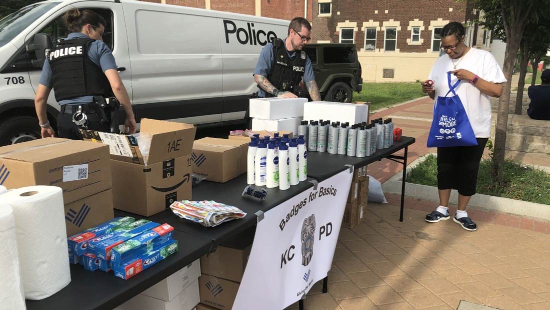 Two police officers handing out personal care items at a table as a person holds a blue bag