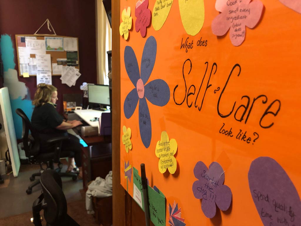An orange board with paper flowers with the words What Does Self Care Look Like?