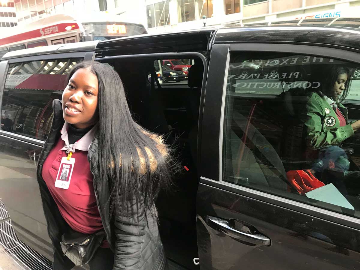 A woman wearing a red shirt and a fur trim hooded jacket exits a van