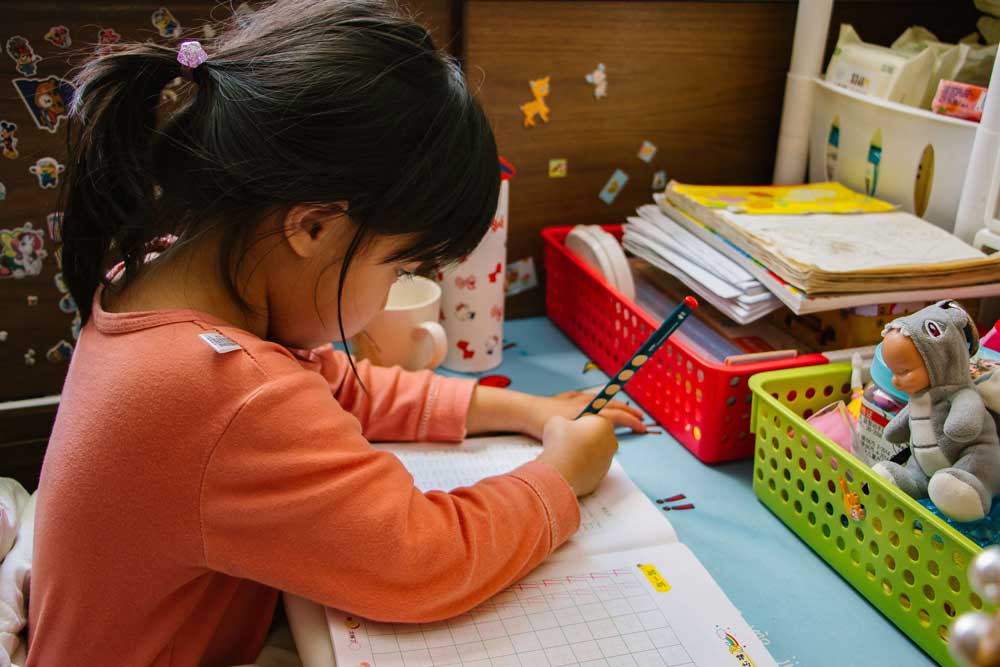 A child in an orange shirt and a ponytail writes in a workbook