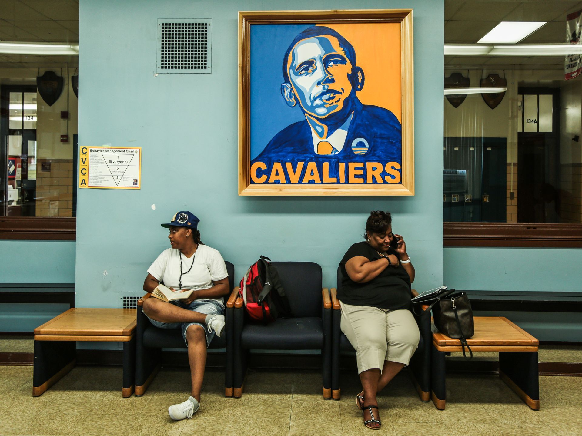 Two people sitting in chairs underneath a portrait of Obama in blue and yellow with the word Cavaliers