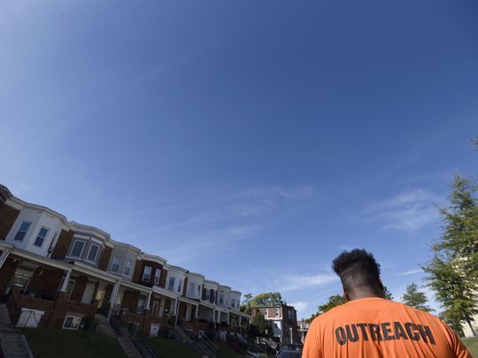 A person wearing an orange shirt with OUTREACH on the back stands in front of Philly rowhomes.