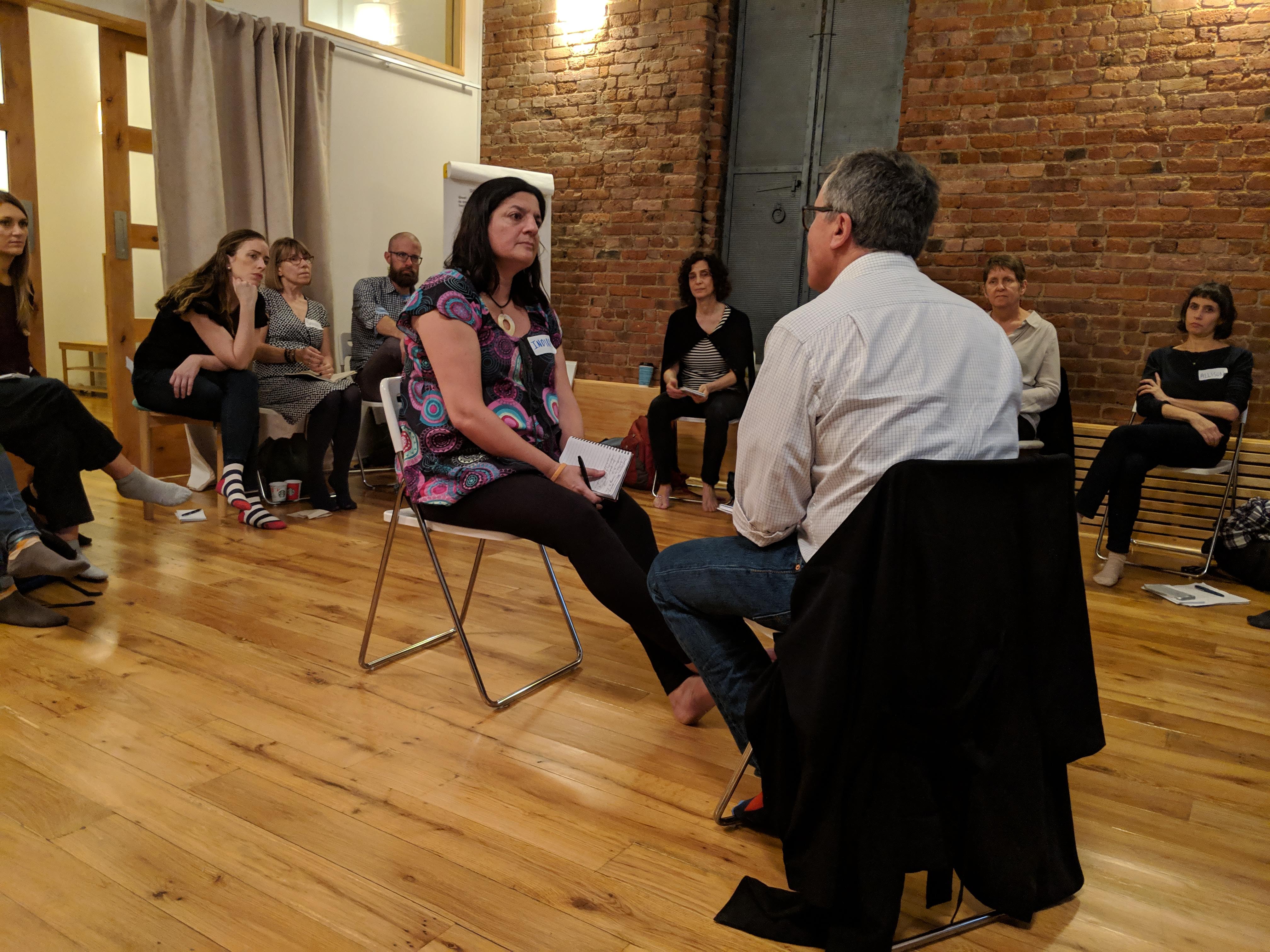 2 people sitting across from each other inside a circle of people seated in chairs