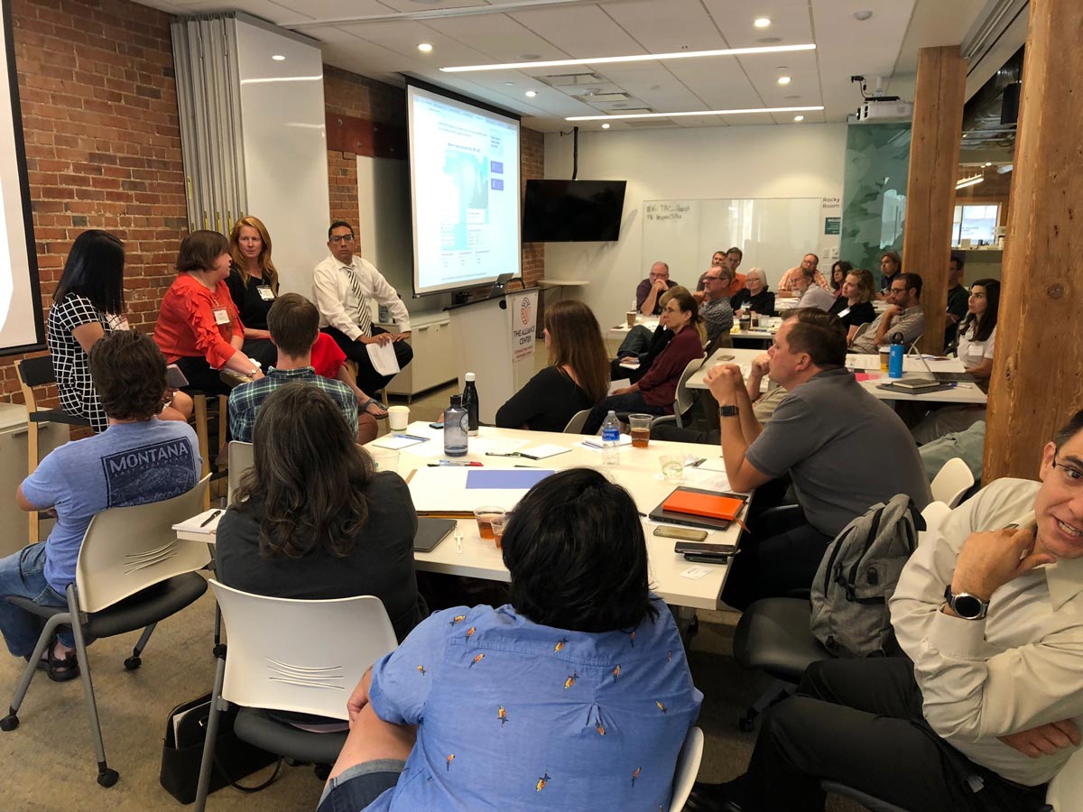 A group of about twenty people in a newsroom meeting