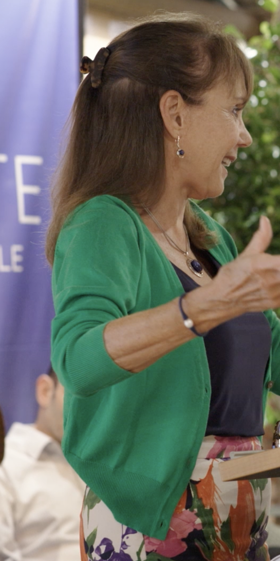 A woman speaks at a podium with her arms open wide