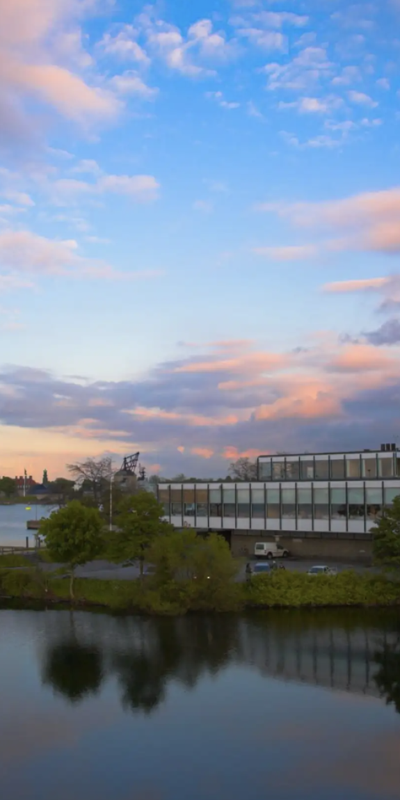 Clouds shine brightly over a modern office building surrounded by trees and water