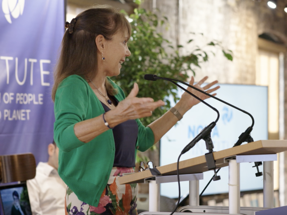 A woman speaks at a podium with her arms open wide