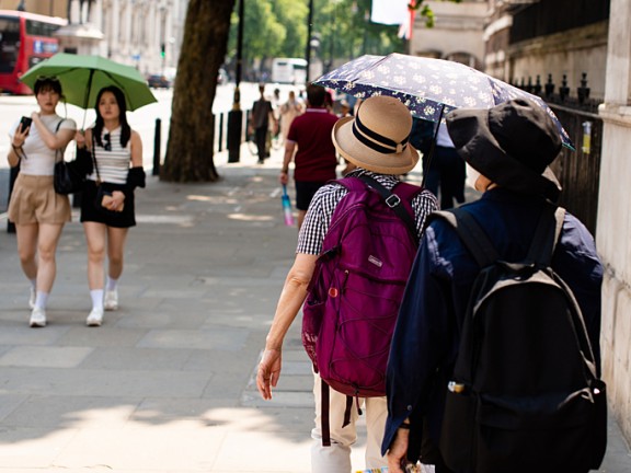 People walk along a street holding umbrellas to protect themselves from the sun