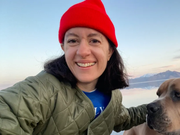 A woman in a bright red hat smiles outside while holding her dog