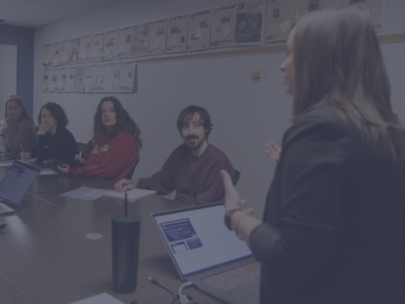 People sit at a long table listening to a speaker