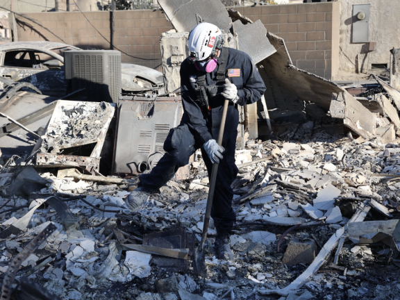 A person in protective gear sifts through debris after the Eaton Fire in Los Angeles County. Photo: CAL FIRE_Official via Flickr Creative Commons