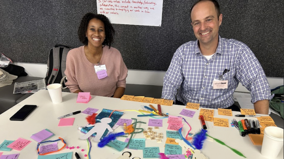 Two Beacon Cohort participants sit at a table covered in sticky notes and pens
