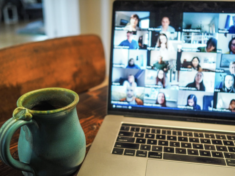 A coffee mug rests on a table next to a laptop screen showing a virtual meeting in progress