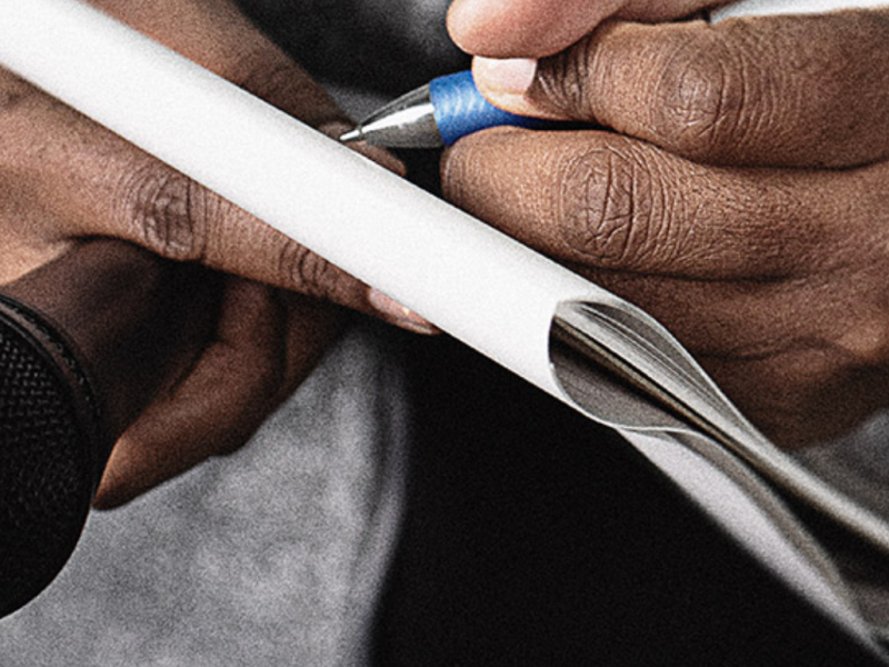 A reporter holds a microphone and takes notes