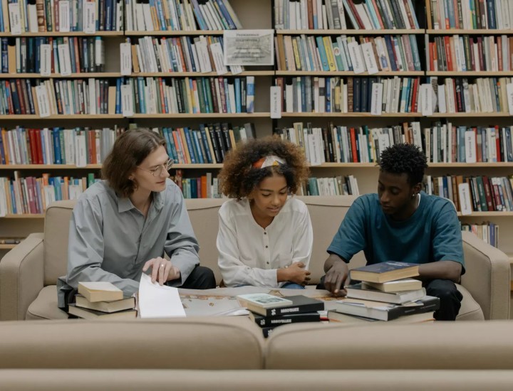 Three students sit on a couch in a library