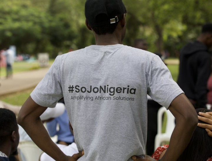 A man stands with hands on hips. His shirt reads "#SoJoNigeria, Amplifying African Solutions"