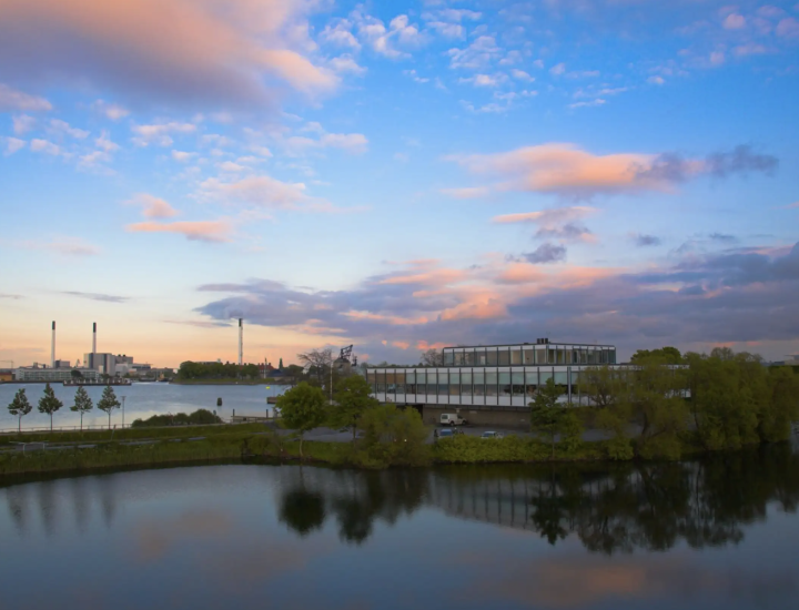Clouds shine brightly over a modern office building surrounded by trees and water