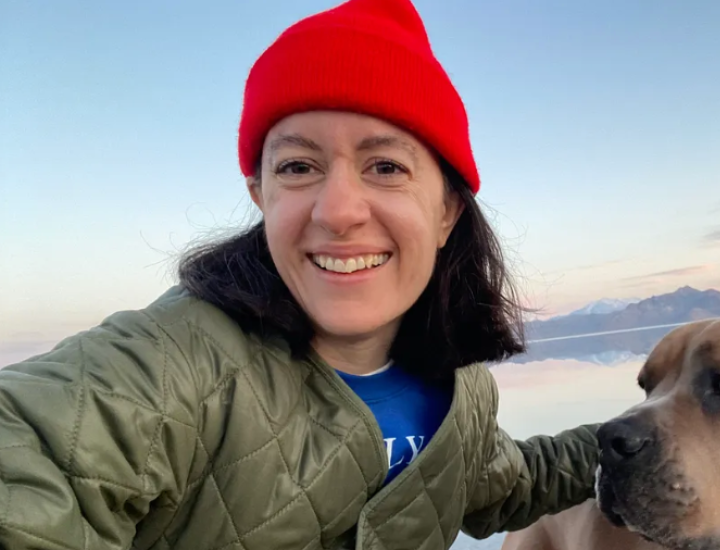 A woman in a bright red hat smiles outside while holding her dog