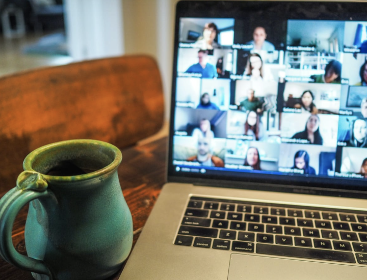 A coffee mug rests on a table next to a laptop screen showing a virtual meeting in progress