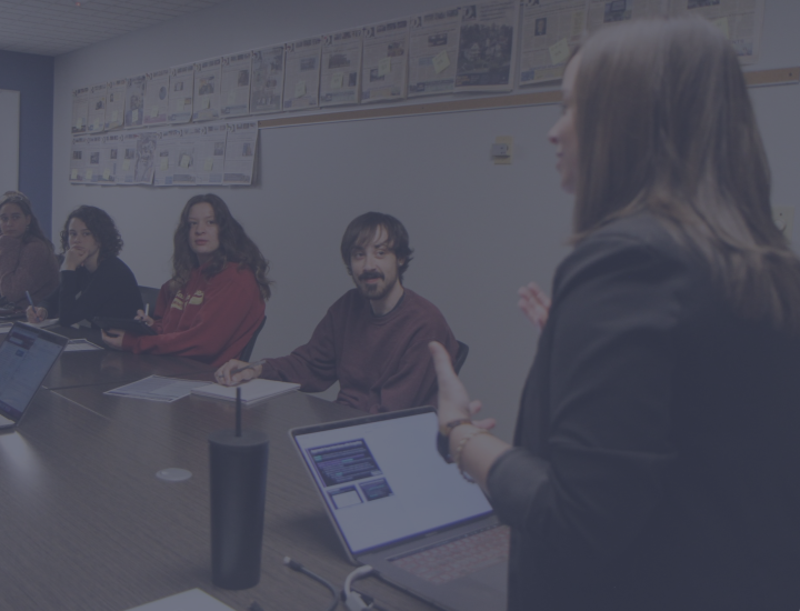 People sit at a long table listening to a speaker