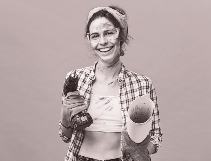A woman holds a power drill and a poster