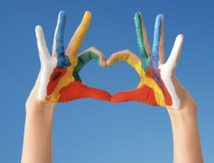 A person makes a heart with their hands, which are painted with bright colors
