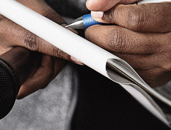 A reporter holds a microphone and takes notes